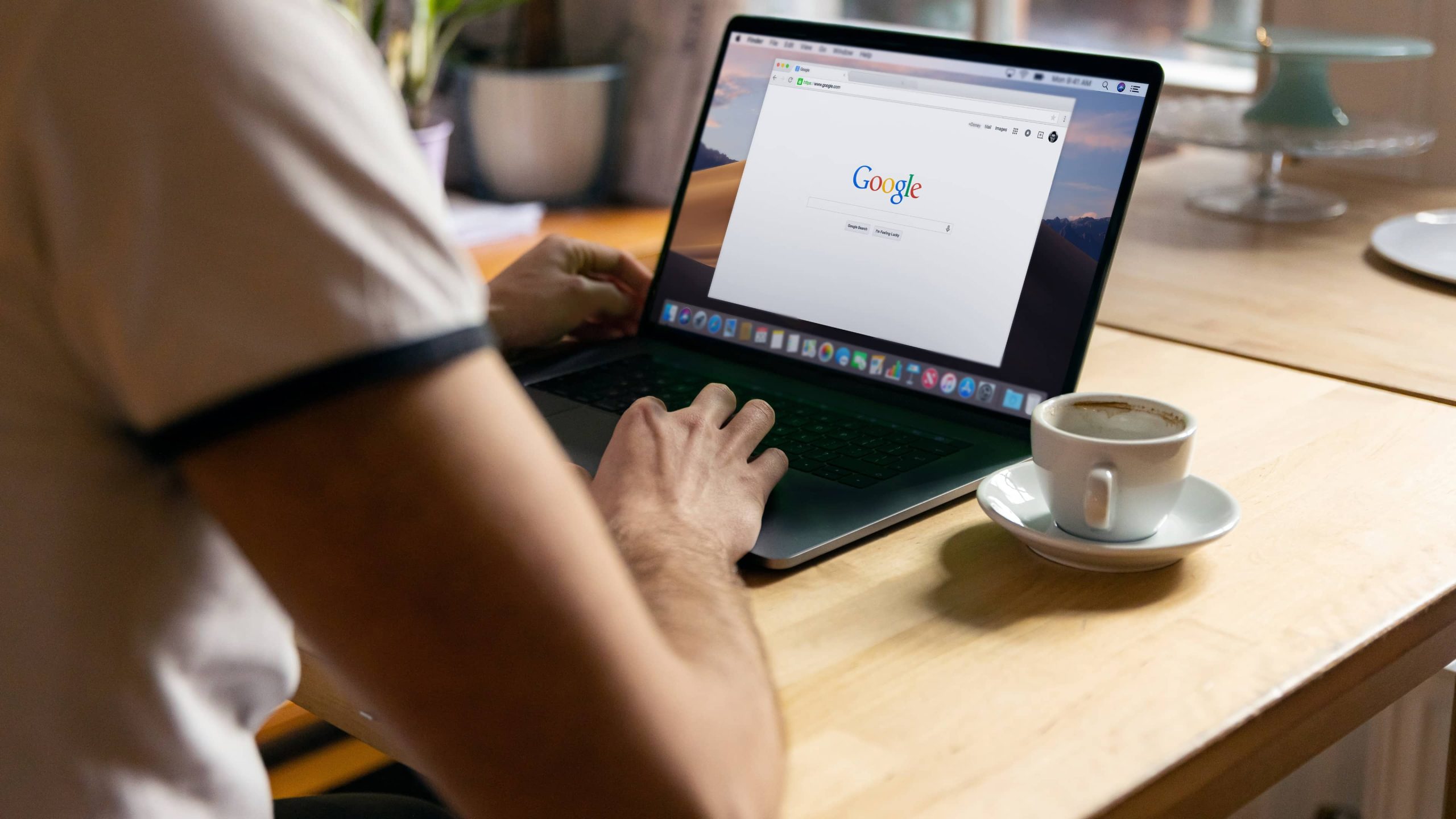 Google arama sayfasında çalışan Chrome tarayıcıyla bir MacBook Pro'nun önünde oturan genç bir erkeği arkadan gösteren bir yaşam tarzı fotoğrafı