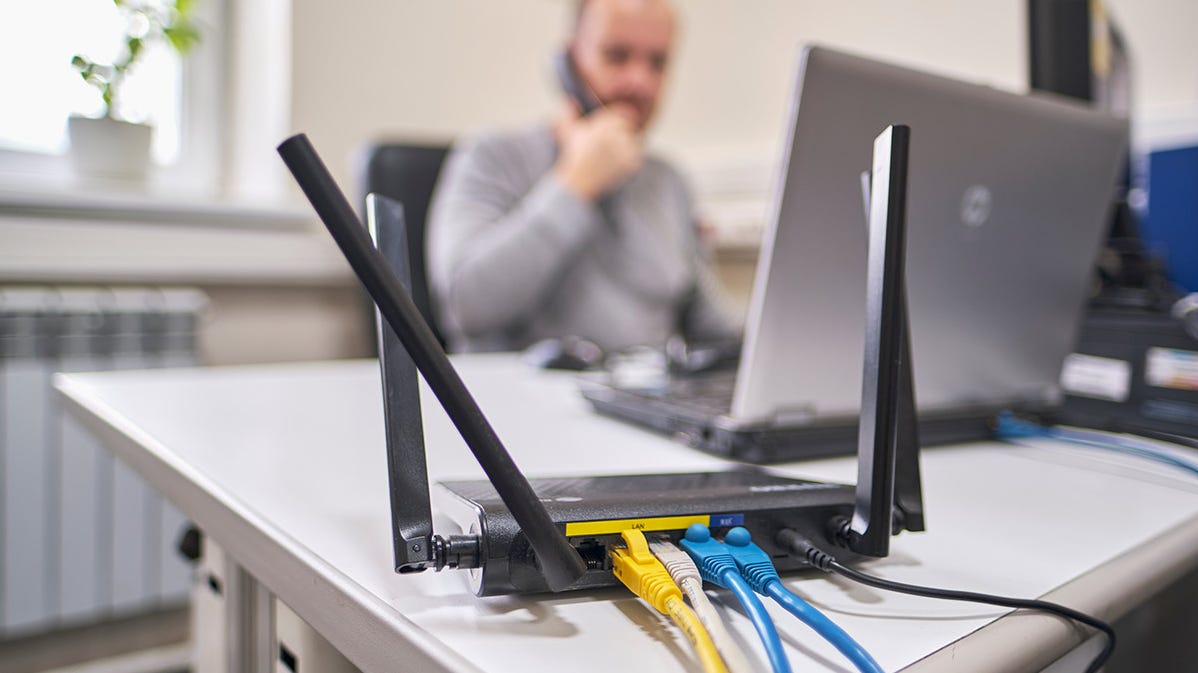 Wi-Fi yönlendiriciye bağlı birden fazla cihazla masada çalışan bir kişi.